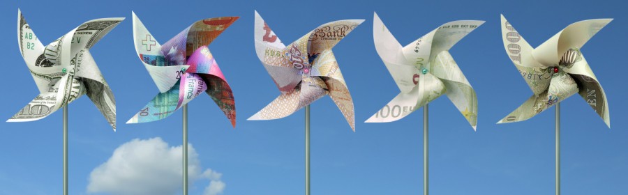 Toy windmills cut from five major world currency banknotes over blue sky, representing finance and financial investment in renewable energy.